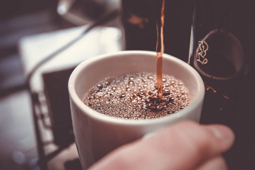 A cup of drip coffee being poured into a white mug