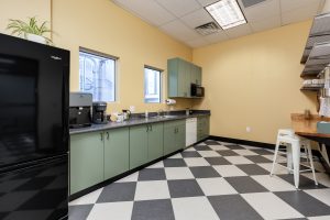 A large, open kitchen with white and black checkered tiles, a lot of counter space, and a black fridge.