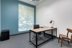 A private office with chairs, a l-shaped wooden desk, and a large window.