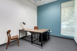 A beautiful private office with large windows and a large l-shaped wooden desk.