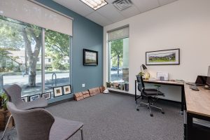 A large private office with one white wall and one teal wall with plenty of large windows.