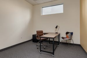 A private office shoes a wooden l-shaped desk, chairs, and a desk lamp.