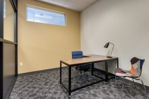 A private office shows a L-shaped wooden desk with a teal chair and desk lamp.
