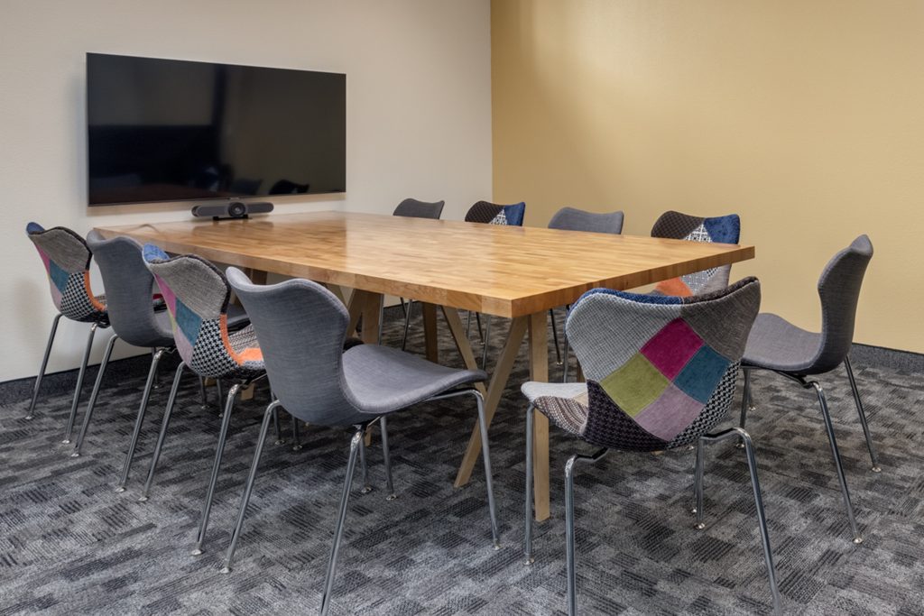 A conference room shows a large television equipped with a web cam. A beautiful wooden table surrounded by chairs.