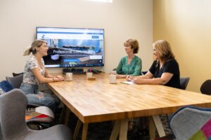 Women sitting around our wooden conference table with a large tv at one end.