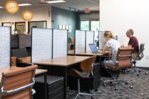 Two members sit at their dedicated desks working on laptops.